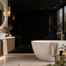 A modern freestanding white bathtub in a luxurious bathroom with a black sparkle wall, gold fixtures, a wooden vanity, and a marble floor.