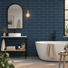 A modern bathroom scene with dark blue subway tile walls, a white freestanding bathtub, a black-framed vessel sink, and a black floor-mounted vanity with a mirror and pendant light.