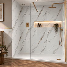 A modern walk-in shower enclosure with a glass door and gold-tone hardware, set in a bathroom with white marble-look walls, a built-in shelf with warm lighting, wood flooring, and small decorative plants.